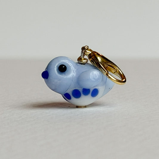 Small blue and white glass bird charm with gold clasp on a light gray background