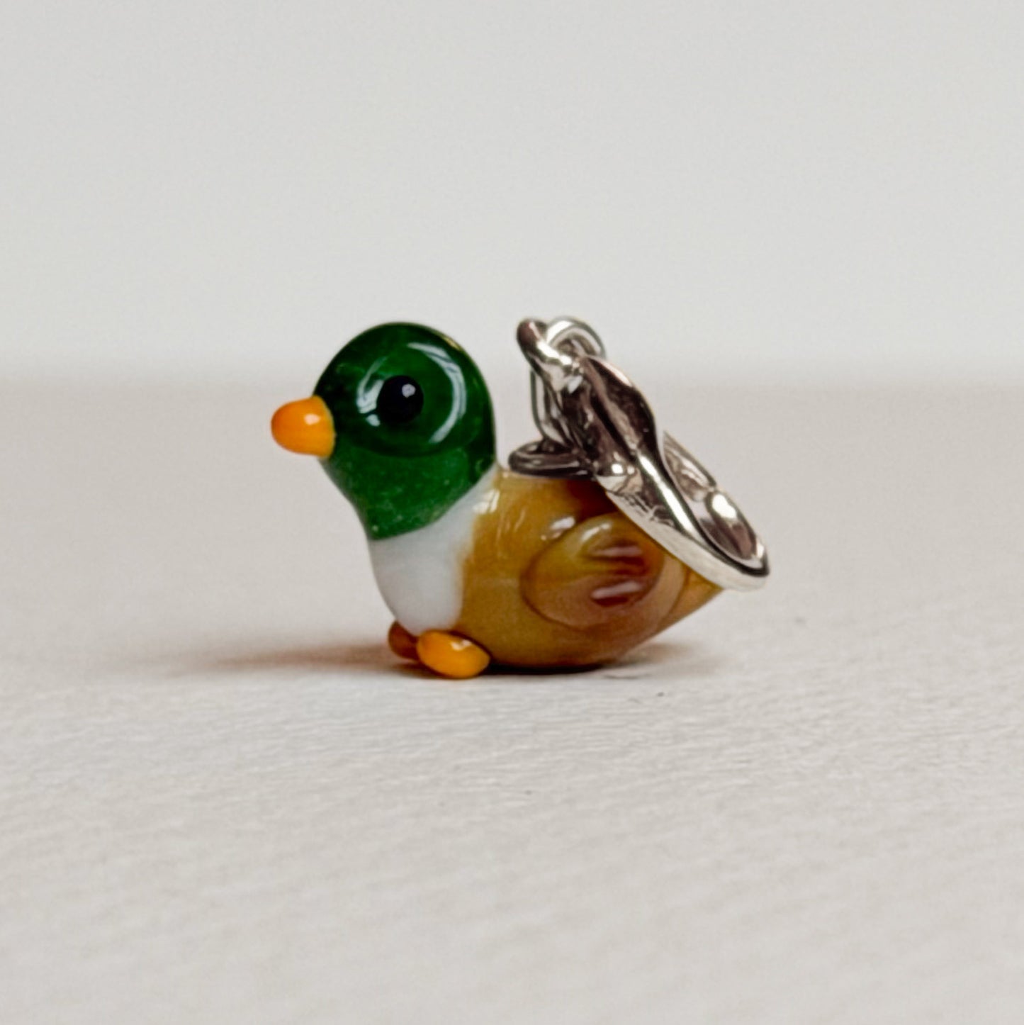 Small duck-shaped charm with silver hardware on a light gray background