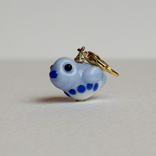 Small blue and white glass bird charm with gold clasp on a light gray background