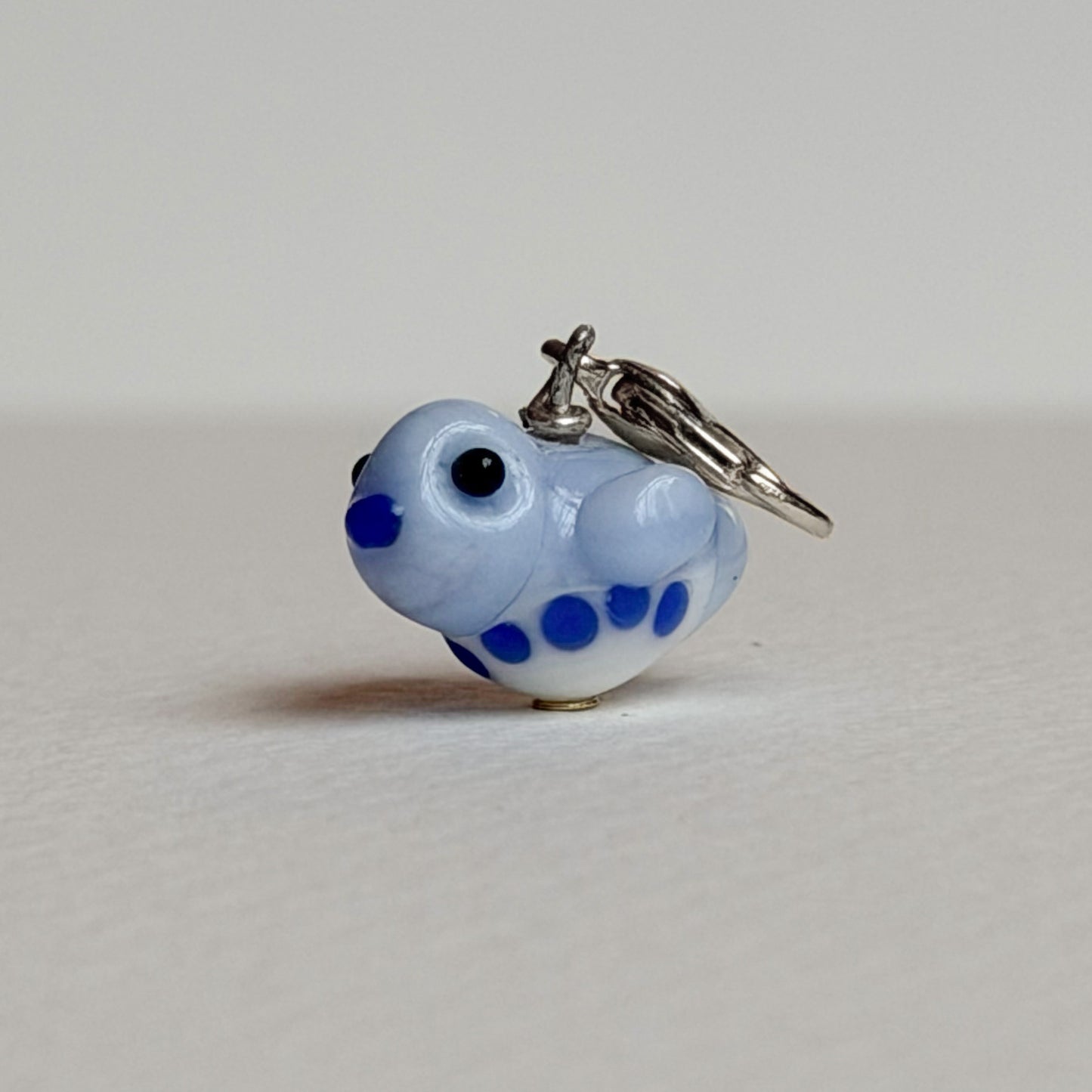 Small blue and white glass bird charm with silver clasp on a light gray background