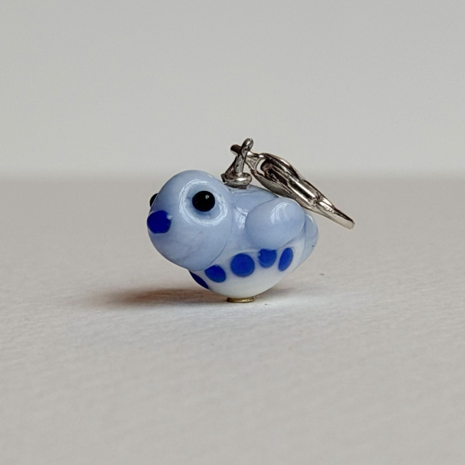 Small blue and white glass bird charm with silver clasp on a light gray background