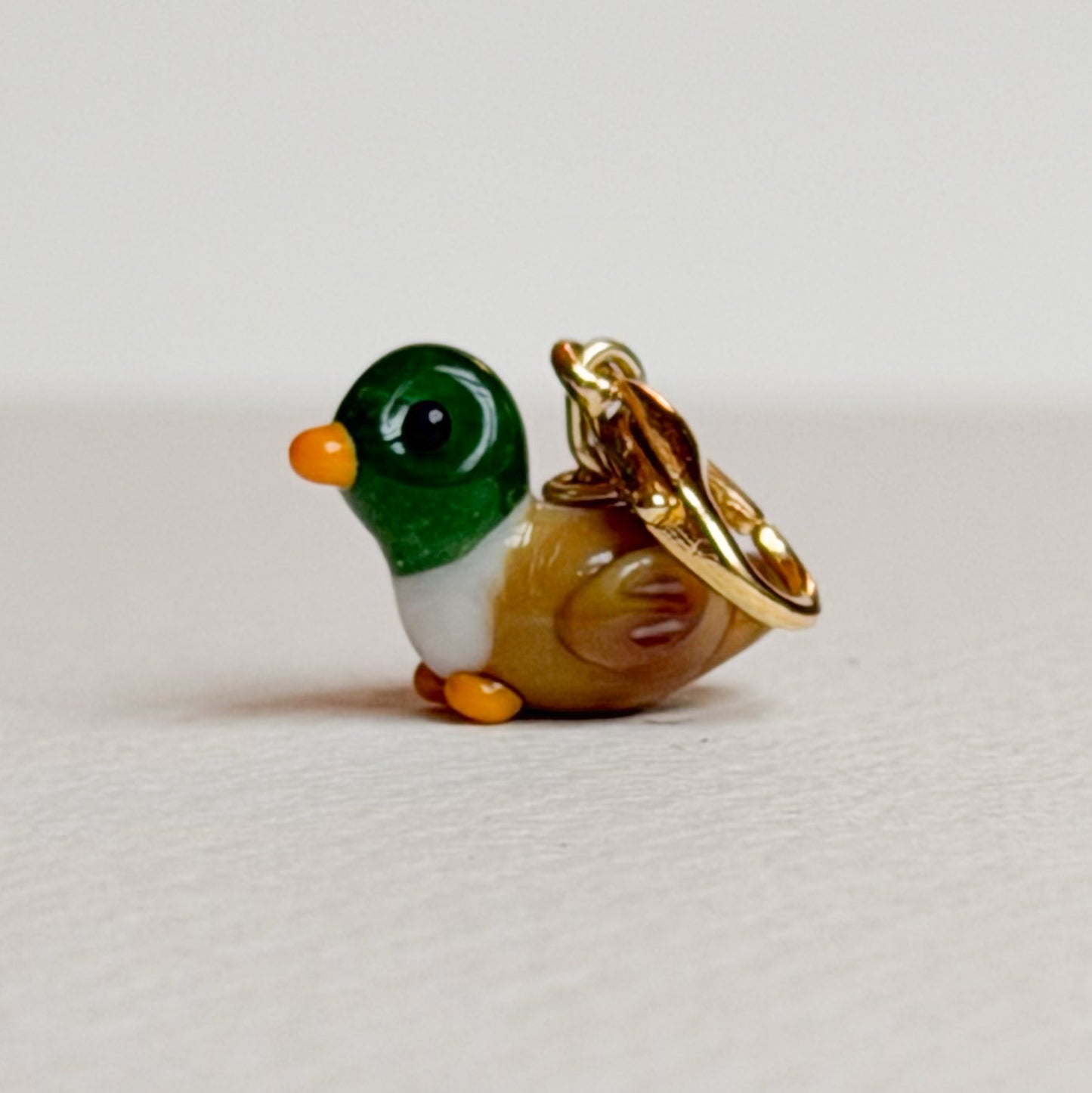 Small duck-shaped charm with gold hardware on a light gray background