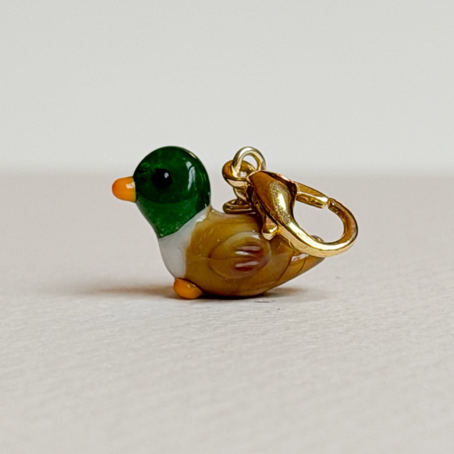 Small duck-shaped charm with gold hardware on a light gray background