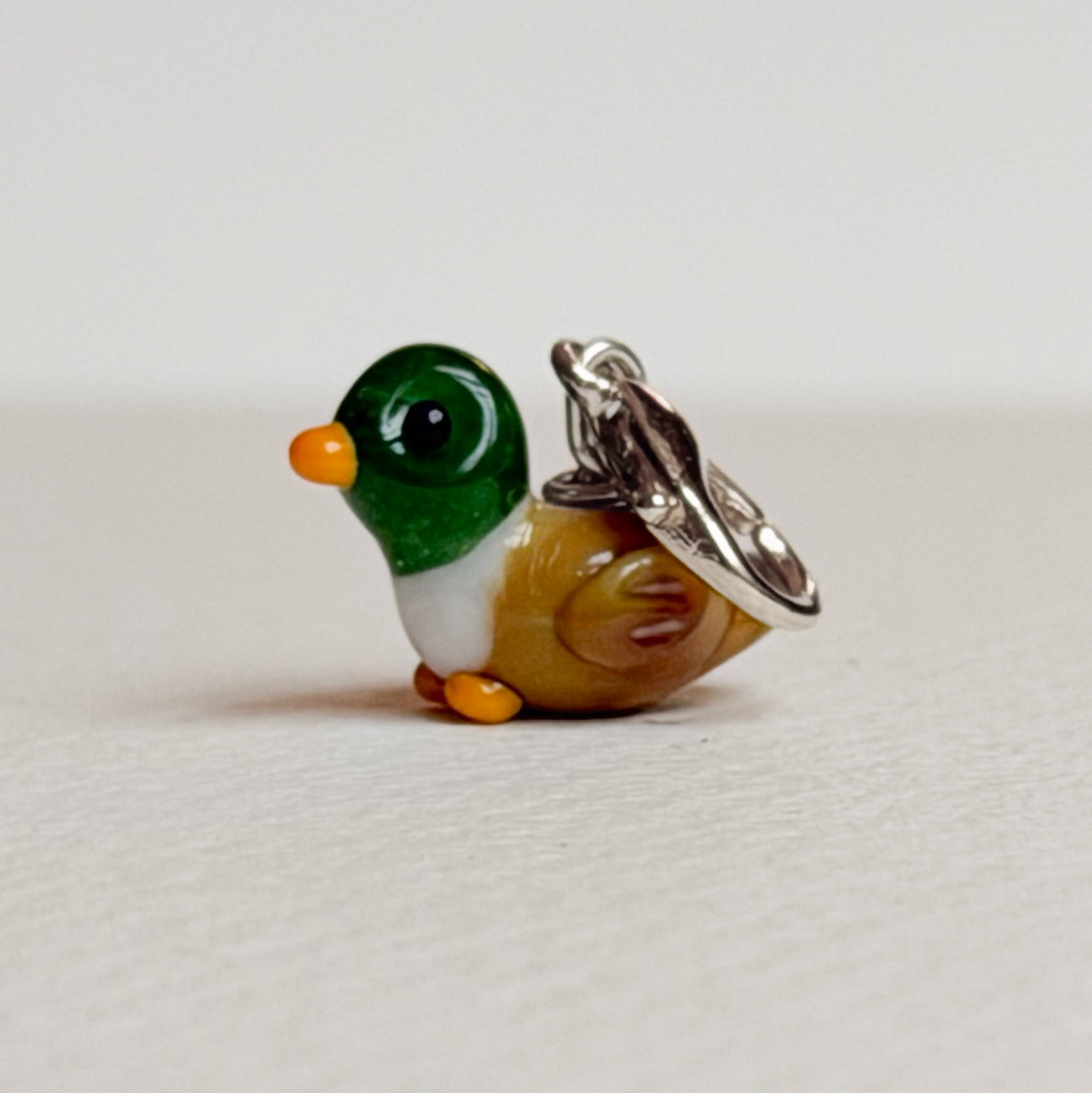 Small duck-shaped charm with silver hardware on a light gray background