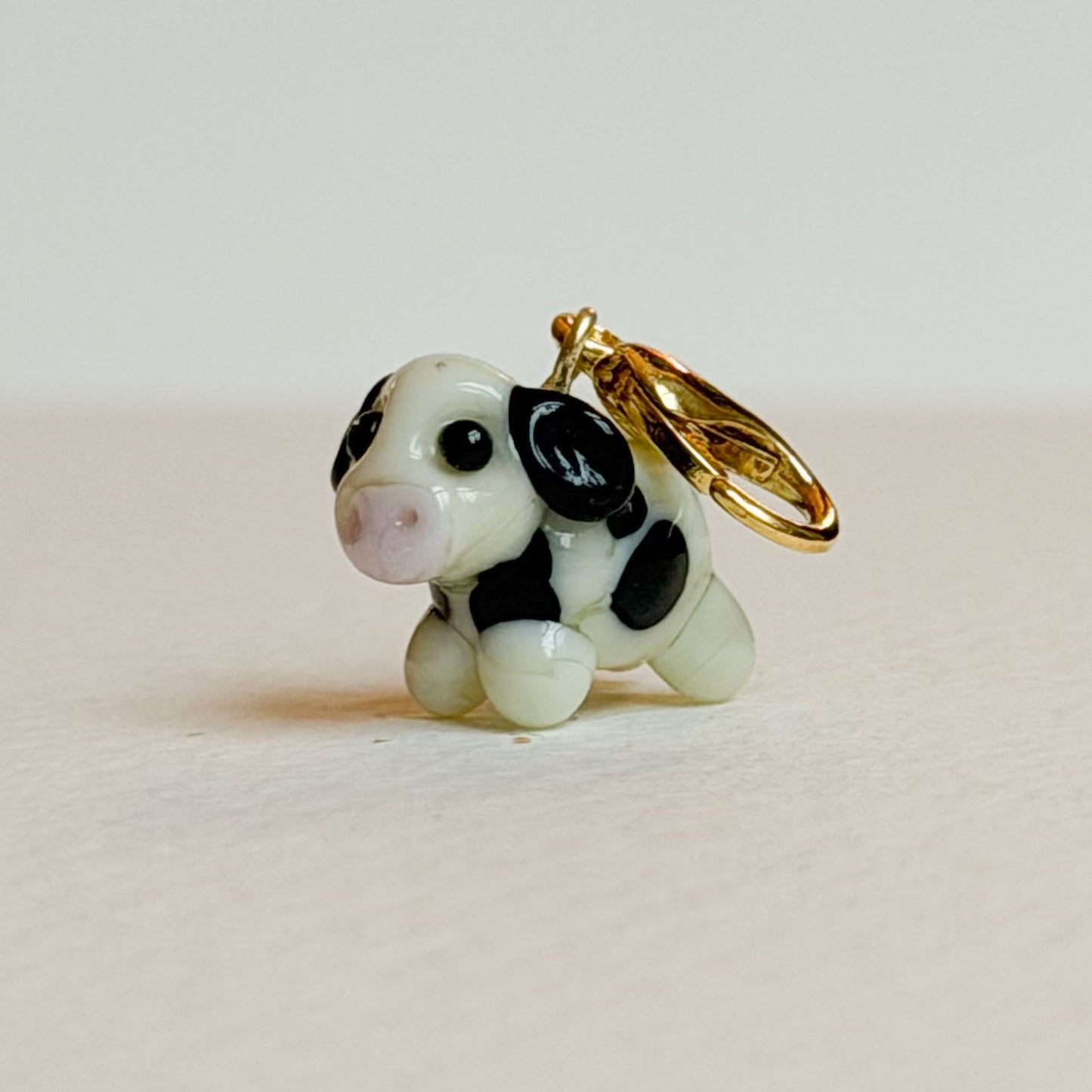 Small cow-shaped charm with a gold ring on a light beige background
