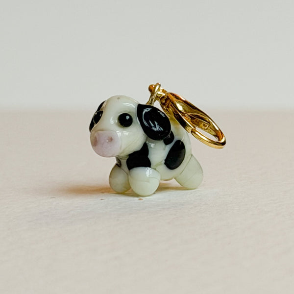 Small cow-shaped charm with a gold ring on a light beige background