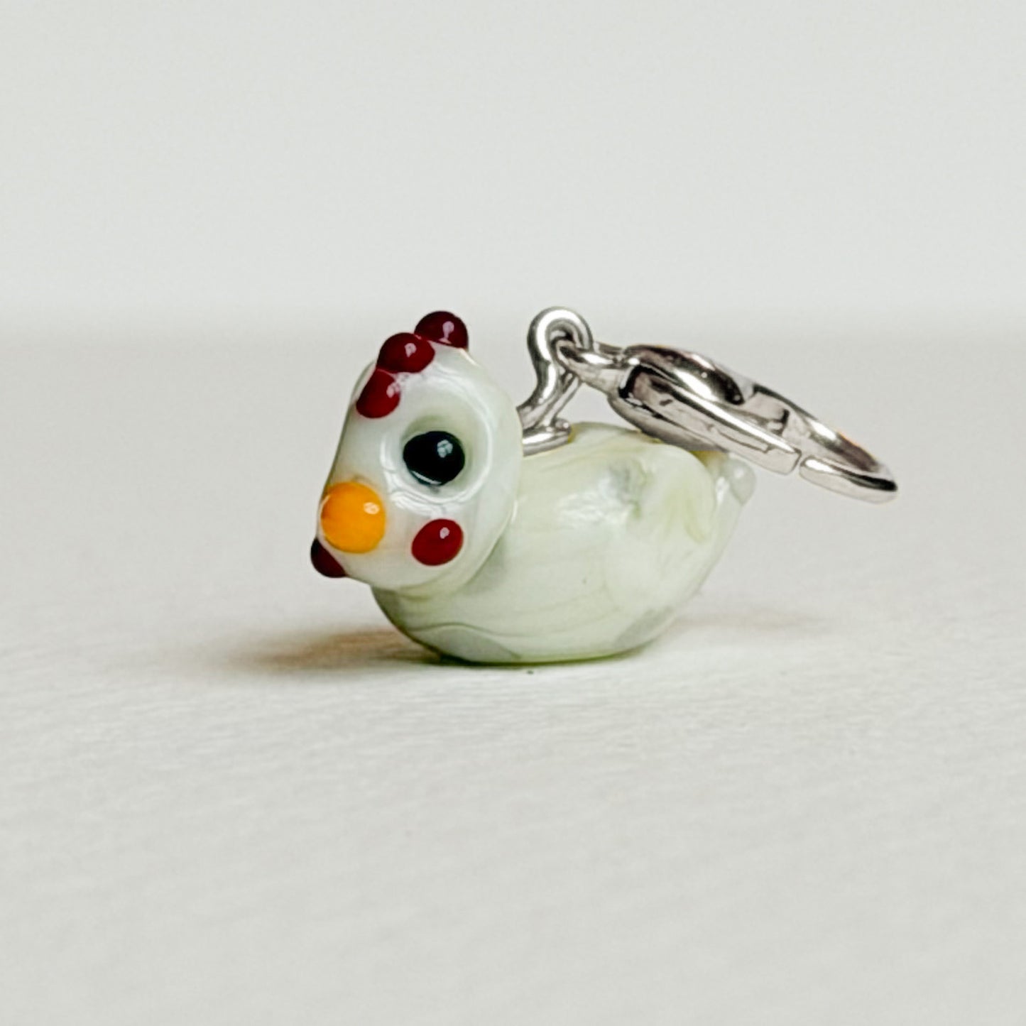 Glass chicken charm with colorful accents on a white background