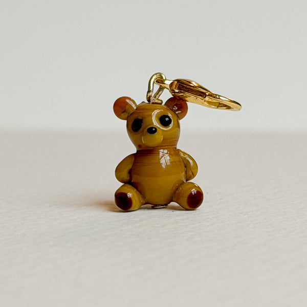 Small teddy bear charm with a gold clasp on a light gray background