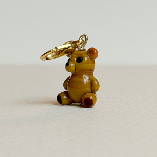Small teddy bear charm with a gold clasp on a light gray background